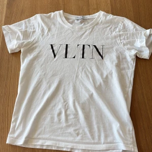 Vit VLTN t-shirt från Valentino - Vit t-shirt från Valentino med svart VLTN-tryck på bröstet. Klassisk rund halsringning och korta ärmar. Den är i storlek S men är rätt så liten i storleken så den passar xs bättre
