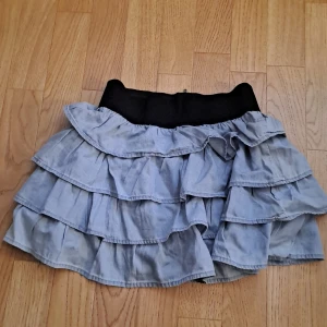 Ljusblå volangkjol  - Supersöt volangkjol från KappAhl i ljusblå bomull med bred svart midjeresår och dragkedja bak. Kjolen har flera lager volanger. 🩷 str 146/152 men passar xs eventuellt även s