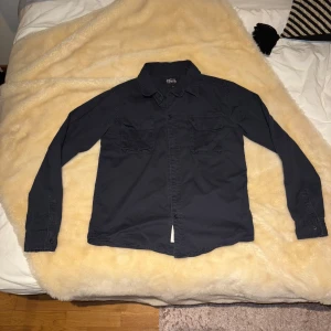 Mörkblå skjortjacka från Native Youth - Snygg mörkblå långärmad skjorta från Native Youth med två bröstfickor och knappar framtill. Perfekt för en stilren look. Skjortan har en klassisk krage och är tillverkad i ett bekvämt material. Perfekt nu för våren! Pris kan absolut diskuteras