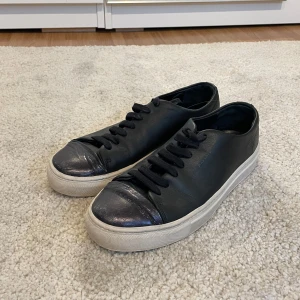 Svarta sneakers från Axel Arigato  - Snygga svarta sneakers från Axel Arigato i läder med svarta snören och vit sula. Den främre delen är en aning glansig och skorna i sig är väll använda med har mycket kvar att ge. Inga större defekter eller likande. Ny priset ligger på 2800 och köpt i deras butik på nk. Storlek 38 men passar mig bra som är 37-38💕