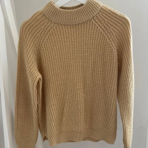 Beige stickad tröja från Vero Moda - Säljer en beige stickad tröja från Vero Moda med grovstickad struktur och hög ribbad krage. Tröjan har långärmad passform och är perfekt för lager-på-lager under kyliga dagar. Enkel och stilren design som funkar till det mesta. Passar även S