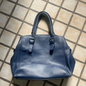 Mörkblå axelväska med blommigt foder - Snygg mörkblå axelväska med både handtag och axelrem. Väskan har en dragkedja på baksidan och insidan är fodrad med ett färgglatt blommigt tyg.🌸