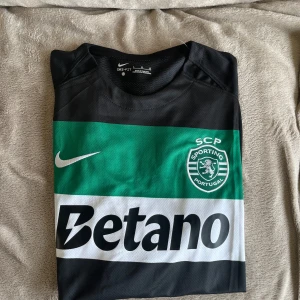 Sporting CP Gyökeres matchtröja Nike - Sporting CP:s officiella matchtröja med Gyökeres och nummer 9 på ryggen. Tröjan är kortärmad och har gröna, svarta och vita breda ränder, klubbmärke och Nike-logga på bröstet samt Betano som sponsor. Tillverkad i lätt och ventilerande polyester.