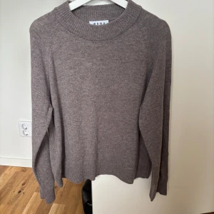 Brun-grå stickad tröja från Wera - Mysig Brun-grå stickad tröja från Wera med rund halsringning och ribbade muddar. Perfekt för lager-på-lager och enkel att matcha med jeans eller kjol. Långärmad och i klassisk, avslappnad passform.