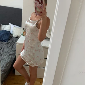 Vit kort klänning med rosa hjärtan - Supersöt vitt kort sovlinne med tunna axelband och rosa hjärtan över hela tyget. Linnet eller mer ”klänning” har en rak passform och är tillverkad i ett glansigt, lätt material som känns svalt mot huden. Perfekt för varma dagar eller när du vill ha en gullig look. Detta är knappt använt, vet tyvärr inte vart de är köpt men jag e rätt säker att de är från Gina/H&M. Storlek S!