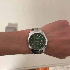 Grön klocka från Doventi med stållänk - Stilren klocka från Doventi med grön urtavla och silverfärgade romerska siffror. Klockan har datumvisning och en robust länk i metall som ger en klassisk känsla. Perfekt accessoar för dig som vill sticka ut med en snygg detalj på handleden.