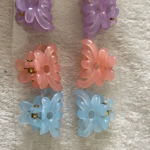 Färgglada blommiga hårklämmor - Säljer ett set med åtta blommiga hårklämmor i pastellfärger: lila, rosa, blå, grön och beige. Klämmorna har en söt blomform och är gjorda i plast med metallfjäder. Perfekta för att piffa upp frisyren med en lekfull och trendig touch. Pris 39kr/3 par /bild 
