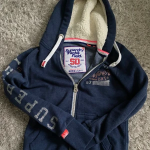 Marinblå Superdry hoodie med teddyfoder - Säljer en marinblå hoodie från Superdry, köpte från plick men var för kort i ärmarna för mig därför säljer jag den. Aldrig andvänd av mig och är i mycket bra skick! Skriv om du har några funderingar. Pris kan diskuteras
