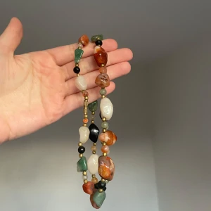 Färgglatt halsband med stora stenar - Hög kvalite Unikt halsband med stora, oregelbundna pärlor i grönt, svart, vitt, brunt och orange. Pärlorna är blandade med små guldfärgade detaljer och har en cool, bohemisk vibe. Perfekt för dig som vill sticka ut med ett statement-smycke.