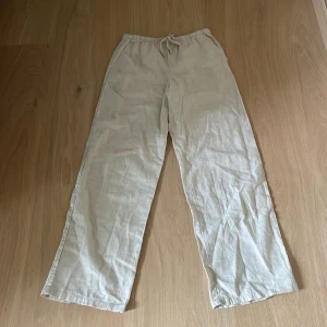 Beige linnebyxor från Gina Tricot - Snygga beige linnebyxor från Gina Tricot med avslappnad passform och dragsko i midjan. Byxorna har raka ben och är perfekta för en chill och stilren look. Lätta och luftiga i materialet, passar grymt till sommaren.