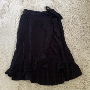 Svart omlottkjol med från Lindex - Svart omlottkjol från Lindex med volangkant och knytband i midjan (se bild)😊Storlek 134/140 men passar mig som har XS. 