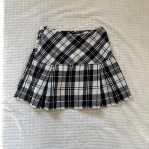 Rutig svartvit kjol från SHEIN XS - Supersnygg kort kjol från SHEIN i svartvitt rutigt mönster. Kjolen har en lätt utsvängd form och dragkedja i sidan för enkel påklädning. Perfekt för dig som gillar en preppy vibe och vill sticka ut lite extra.