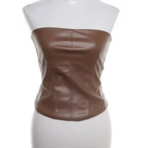 Brun skinnkorsett  - Säljer en brun korsett-topp i skinnimitation från Stradivarius. Toppen är axelbandslös och har markerade sömmar framtill för en snygg form. Dragkedja bak för enkel påklädning. Perfekt till utrkvällar✨✨