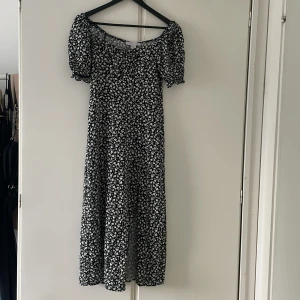 Svart blommig långklänning från Amis - Supersöt svart långklänning från Amis med vita blommor, puffiga korta ärmar och smockad överdel. Klänningen har en romantisk vibe och är perfekt för varma dagar. Lätt och flowy i materialet, med en feminin siluett och rundad halsringning.