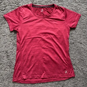 Röd tränings-tshirt från SOC - Sportig röd t-shirt från SOC med rund hals och korta ärmar. Tillverkad i ett lätt och ventilerande syntetmaterial, perfekt för träning. Snygg diskret mönstring och reflexdetalj på ryggen för extra synlighet.