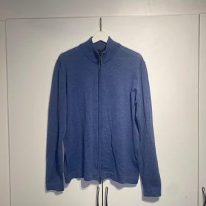 Oscar Jacobson fullzip i merinoull - Snygg blå fullzip från Oscar Jacobson i 100% mjuk merinoull. Modellen har hel dragkedja framtill, ribbad krage och långa ärmar. Perfekt för lager-på-lager och passar till både jeans och chinos. Enkel och stilren design som funkar året runt. Enormt bekväm och sparsamt använd. Nypris 1900kr. 