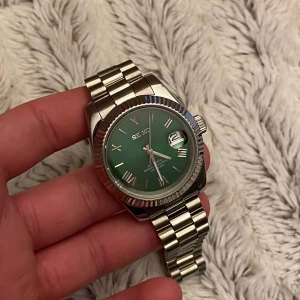 Grön Seiko Datejust Mod - Tvär snygg Seiko-mod klocka med grön urtavla och romerska siffror. Den har en silverfärgad metallarmband och en datumvisare. Perfekt för dig som vill ha en stilren och iögonfallande accessoar. Alla länkar tillkommer vid köp. Klockan är automatisk med en NH34 movement. Om det är några frågor är det bara att ställa dem privat!