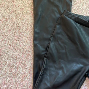 Svarta skinnbyxor från XOXO - Snygga svarta skinnbyxor från XOXO. Perfekta för en trendig look med en tight passform. Byxorna har en elastisk midja för extra komfort och stil.