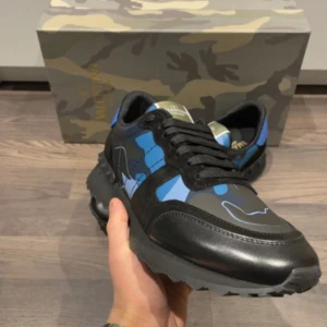 Svarta och blå sneakers från Valentino - Snygga sneakers från Valentino i svart och blått med ett coolt camouflagemönster. Skorna har snörning och en robust sula som ger bra grepp. Perfekta för att ge din outfit en edgy touch.