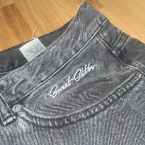 Grå jeans från Sweet Sktbs - Snygga grå jeans från Sweet Sktbs med broderad detalj på bakfickan. De har en klassisk femficksdesign och en knappgylf. De är ganska slitna längst ner!