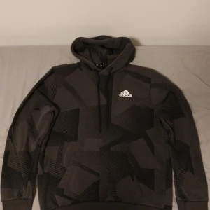 Svart/Grå tracksuit från Adidas - Säljer en svart/grå tracksuit från Adidas med ett geometriskt mönster. Tracksuiten är lite loose av sig, hängig och bra för en avslappnad stil.