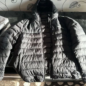 Svart pufferjacka från Champion - Säljer en svart pufferjacka från Champion med dragkedja och huva. Jackan har ett quiltat mönster och är långärmad. Perfekt för kyligare dagar.