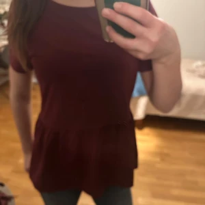 Vinröd topp med volangdetalj - Säljer en söt vinröd topp med volangdetalj i nederkant. Har endast används 3 gånger ❤️är storlek  158/164 men skulle säga att den passar som en xs/s🥰