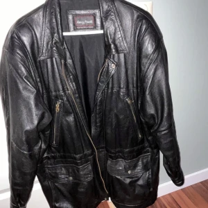 Svart skinnjacka från Henry Morell - Säljer en svart skinnjacka från Henry Morell. Jackan har en klassisk design med dragkedja och flera fickor med dragkedjor framtill. Perfekt för en cool och tidlös stil.