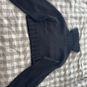 Svart croppad polotröja - Snygg svart croppad polotröja med ribbade detaljer vid hals och nederkant. Perfekt för en stilren look och passar bra till både jeans och kjol.