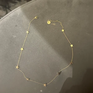 Guldhalsband med stjärnor - Elegant guldhalsband dekorerat med små stjärnor längs kedjan. Perfekt för att lägga till en subtil glans till din outfit. Justerbar längd med en liten berlock vid låset.