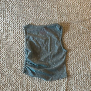 Glittrig fest topp - Säljer en snygg glittrig topp i blått. Perfekt för en kväll ute eller en festlig tillställning. Toppen har en stilren design med en glittrig yta och en fin passform. 