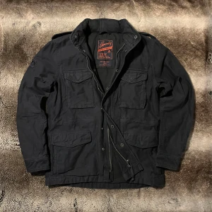 Superdry Feild jacka  - Säljer denna svarta M65 Feild Jacket från Superdry. Jackan är vintage från en av deras äldre kollektioner och har en stilren design. Skriv om ni undrar något!