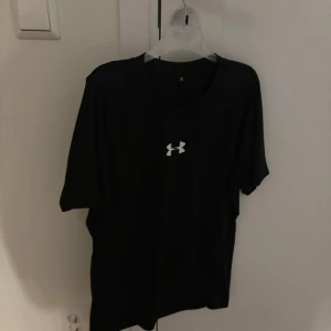 Svart compression shirt från Under Armour - Säljer en svart compression shirt från Under Armour med korta ärmar och deras ikoniska logga på bröstet. Perfekt för träning eller vardagsbruk. Skön passform och stilren design.