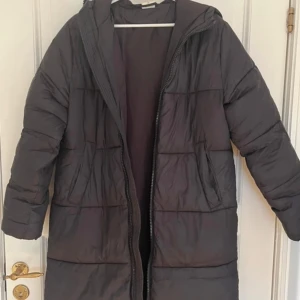 Svart dunjacka från Kangol - Säljer en svart dunjacka från Kangol med huva och dragkedja. Jackan har långa ärmar och två stora fickor framtill. Perfekt för kalla dagar.