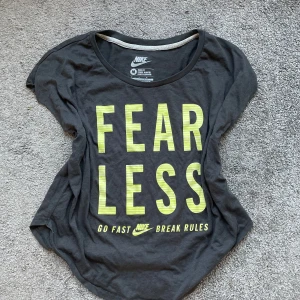Svart tränings t-shirt från Nike med text - Säljer en svart t-shirt från Nike med texten 'FEARLESS' i gult på framsidan. Under texten står det 'GO FAST BREAK RULES'. T-shirten har en rund halsringning och korta ärmar. Perfekt för en sportig look! Öppen för prisförslag!