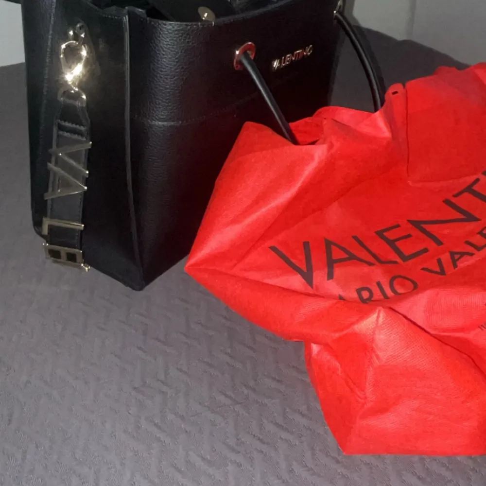Snygg svart handväska från Valentino med elegant design. Väskan har två handtag och en justerbar axelrem med gulddetaljer. Insidan är rymlig med flera fack och dragkedjor för enkel organisering. Perfekt för att bära dina dagliga nödvändigheter med stil. Knappt använd . Laukut & Käsilaukut.