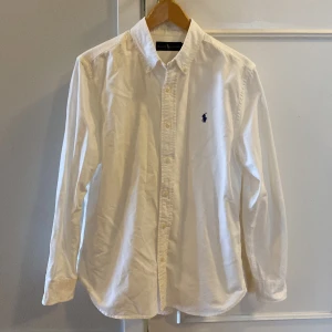 Vit skjorta från Ralph Lauren - Klassisk vit skjorta från Ralph Lauren med broderad logga på bröstet. Skjortan har långa ärmar och knappar framtill. Perfekt för en stilren look. Pris kan diskuteras vid snabb affär!