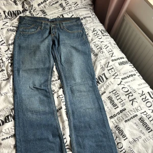 Blå jeans från Stone - Snygga blå jeans från Stone med klassisk femficksdesign och kontrastsömmar. De har en knappgylf och bälteshällor, vilket gör dem perfekta för en avslappnad stil. Jeansen har en rak passform som ger en tidlös look. Jätte lågmidjade, står ej storlek men skulle gissa på 27-28/32. Vid köp av flera plagg går jag ner i pris
