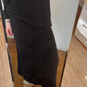 Svart stickad långkjol - Snygg och bekväm svart stickad långkjol perfekt för kyligare dagar. Kjolen har en enkel design som gör den lätt att matcha med olika toppar. Den stickade texturen ger en mysig känsla.