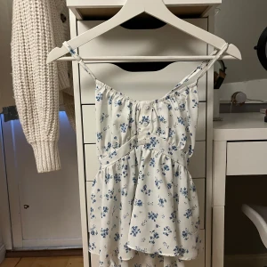 Vit blommig linne - Söt vit blus linne med blå blommor och smala axelband. Perfekt för varma dagar med sin lätta och luftiga design. Den har en slags rosett knytning i ryggen💓💓