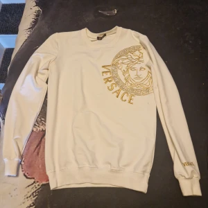 Röd hoodie från GANT - Säljer en snygg röd hoodie från GANT med logga och emblem på bröstet. Den har en praktisk känguruficka och justerbar huva med snörning. Perfekt för en avslappnad stil.