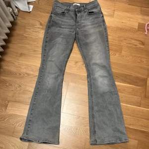 Grå bootcut jeans - Snygga ljusgrå bootcut jeans med en klassisk femficksdesign. De har en knapp och dragkedja framtill. Perfekta för en avslappnad stil med en modern twist. Byxorna är från Gina Tricot i storlek 38. De har även en liten smutsfläck under knät som ni ser på en av bilderna. Den syns bara om man ”letar efter den”.
