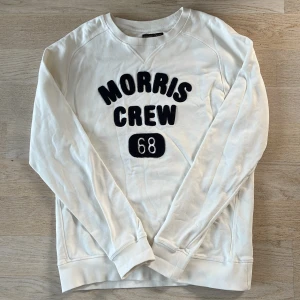 Vit sweatshirt från Morris Gents - Säljer en stilren vit sweatshirt från Morris Gents med texten 'Morris Crew 68' i svart på framsidan. Tröjan har långa ärmar och en klassisk rund halsringning. Perfekt för en avslappnad stil.