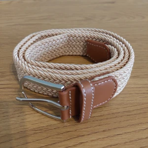 Beige flätat bälte med bruna detaljer - Snyggt beige flätat bälte med bruna skinn-detaljer och en stilren silverfärgad spänne. Perfekt för att ge en avslappnad men ändå stilren look. Passar till många olika outfits och tillfällen.