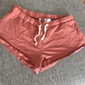 Lågmidjade Rosa shorts från H&M - Säljer ett par bekväma rosa shorts från H&M. De har en elastisk midja med vit snörning för justerbar passform. 