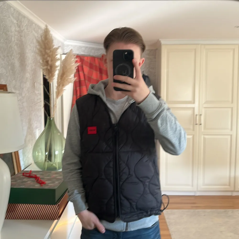 Säljer en svart quiltad väst från Hugo med röd insida. Västen har dragkedja framtill och en justerbar dragsko i nederkant. Perfekt för lager-på-lager under kyligare dagar. Nypris:1200. Takit.