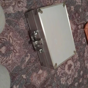 Silverfärgad sminkväska typ - Säljer en stilren silverfärgad portfölj med metallhörn och ett robust handtag. Perfekt för att förvara viktiga dokument eller småprylar. Den har en säker låsmekanism och en enkel design som passar alla tillfällen.