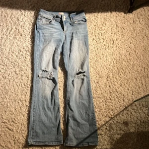 Ljusblå bootcut jeans från Nelly - Snygga ljusblå bootcut jeans från Nelly med slitna detaljer på knäna. De har en klassisk femficksdesign och knappar bak på fickorna. Perfekta för en avslappnad stil.