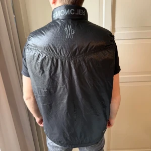 Svart quiltad väst - Snygg svart quiltad väst med dragkedja framtill. Perfekt för lager-på-lager och ger en stilren look. Västen har en modern design med tryck på kragen och ryggen. Pris kan diskuteras vid snabb affär. Storlek L men passar bra för dom med storlek M också.