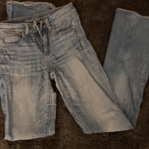 Blå jeans från American Eagle - Snygga blå jeans från American Eagle med en klassisk femficksdesign och som är superstretchiga. De har en dragkedja och knapp framtill. Perfekta för en avslappnad stil. Det finns även en liten reva vid låret. 